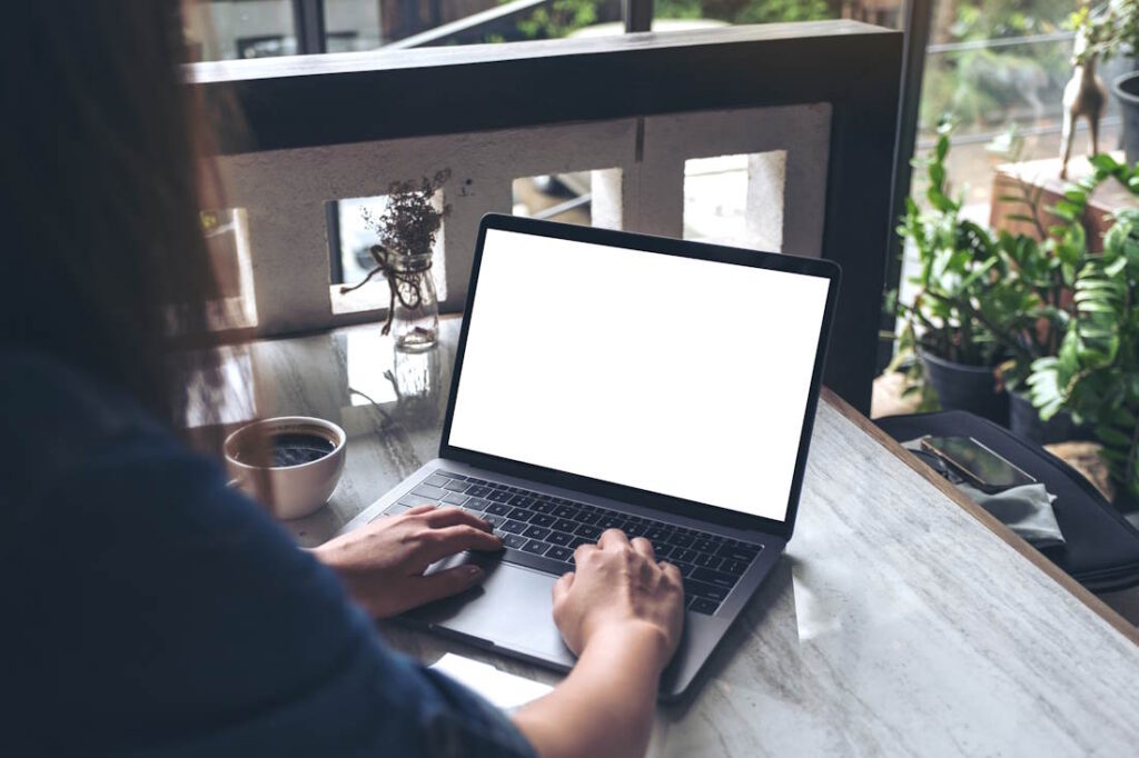 Mockup image of a woman using laptop with blank white desktop screen with coffee cup on table